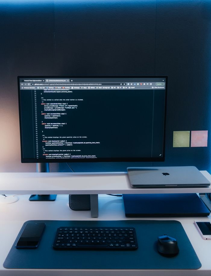 Minimalist home office desk setup with coding on a large monitor, laptop, and gadgets.