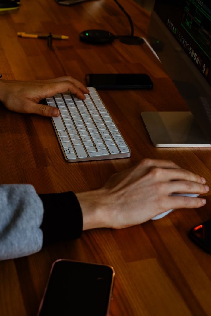 Close-up of hands typing and using a mouse on a modern desk with a keyboard and monitor.